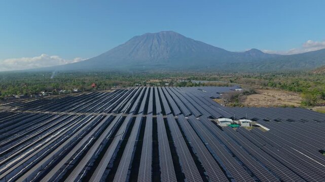 Aerial view of PLTS Bali Timur solar farm with rows of photovoltaic panels set against a backdrop of a majestic volcano in Kubu, Bali, Indonesia.