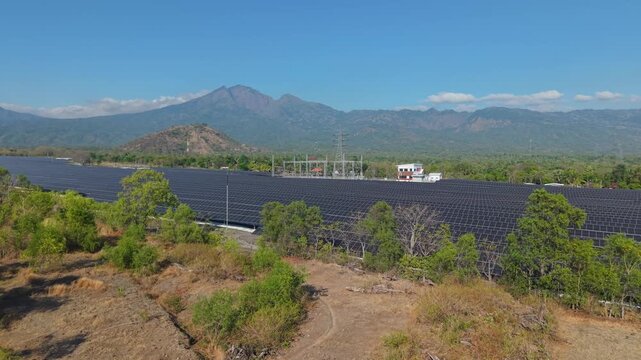 Aerial view of PLTS Bali Timur solar farm with rows of solar panels and surrounding lush vegetation under a clear blue sky in Kubu, Bali, Indonesia.