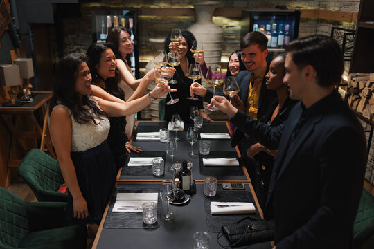 Group of diverse people, six friends having a nice time together, enjoying dining at a luxury modern restaurant and cheering with wine.
