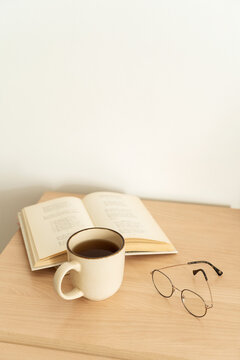 Book lies open on wooden table with mug Hot tea and reading glasses create cozy and calm atmosphere. Slow living, mindful time. Relaxing morning with book and hot tea