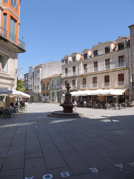 View of the historic Fonte da Praza de Curros Enriquez in a sunny square surrounded by traditional stone buildings with balconies and outdoor cafe seating in Pontevedra, Pontevedra, Spain.