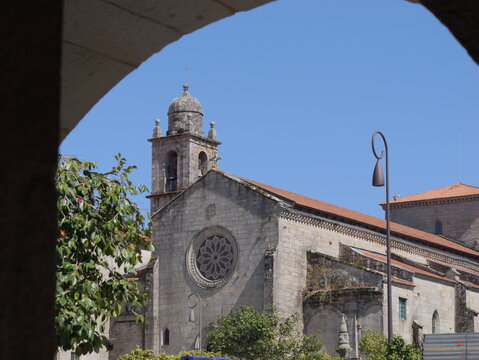 View of the Convento e Igrexa de San Francisco with its stone facade, rose window, and bell tower framed by an archway under a clear blue sky in Pontevedra, Pontevedra, Spain.