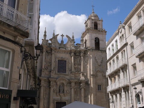 View of Igrexa da Santa Eufemia with its ornate baroque facade and bell tower, framed by historic stone buildings under a blue sky in Ourense, Ourense, Spain.