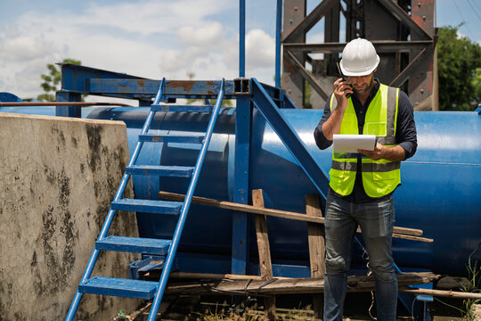 Focused professional female civil engineer holding a clipboard while inspecting large water gate infrastructure for flood control and environmental safety during an active outdoor operation.