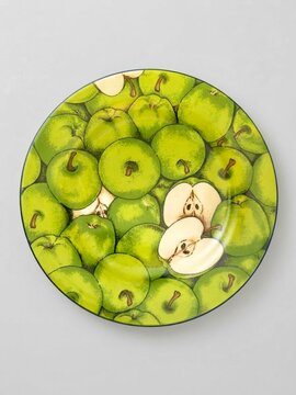 Vintage decorative ceramic plate featuring detailed green apple pattern illustration, overhead top view on plain light grey studio background, ideal for kitchen art print and dining table decor
