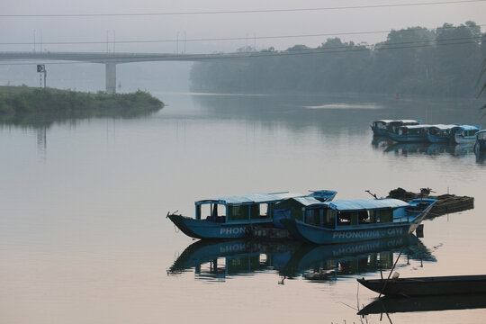 Scenic view of traditional blue tourist boats moored on the calm foggy Son River with a concrete bridge in the background in Phong Nha, Vietnam on January 18, 2026.
