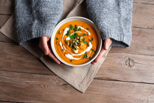 Female hands in knitted sweater holding bowl with pumpkin soup