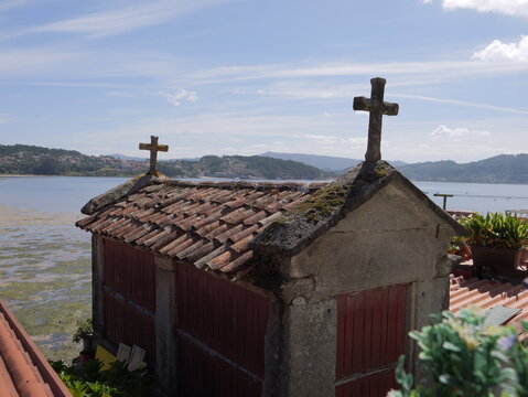 View of a traditional stone horreo with crosses on its tiled roof overlooking the estuary in Combarro, Pontevedra, Spain.