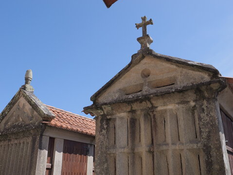 View of traditional stone granaries with crosses on top and tiled roofs under a clear blue sky in Combarro, Pontevedra, Spain.