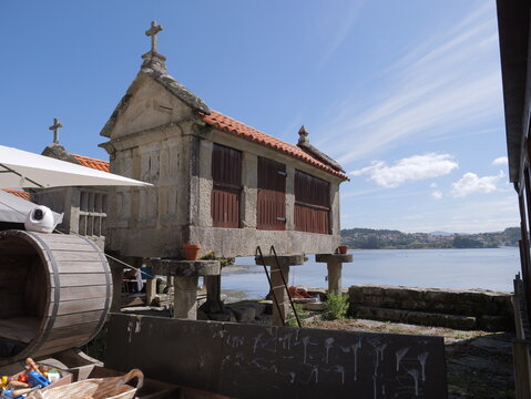 View of a traditional stone horreo with wooden doors and a cross on top, situated along the coastal waterfront in Combarro, Pontevedra, Spain.