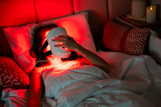 Woman using Led Red Light Facial Mask in the bed