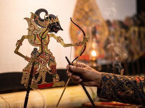 Dalang hand holding Arjuna Wayang Kulit archer puppet with bow in front of kelir screen