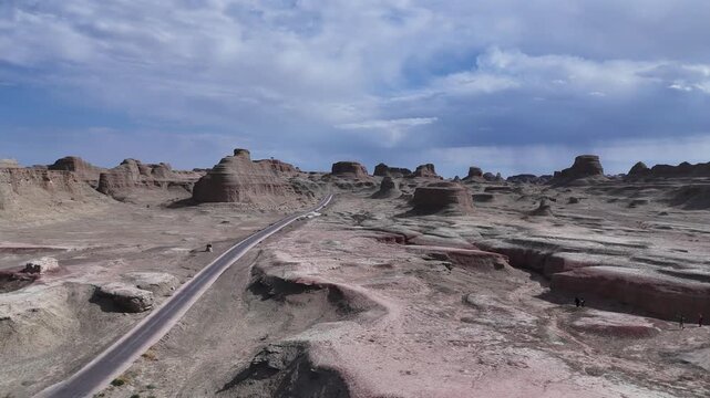 A road winding through the "Devil's City" in the Urho District of Karamay, Northern Xinjiang, China&mdash;a landscape of rocky desert terrain featuring strange formations resembling towers and animals.
