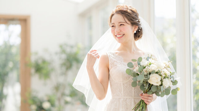 ウェディングドレスを着てブーケを持ち微笑む若い新婦