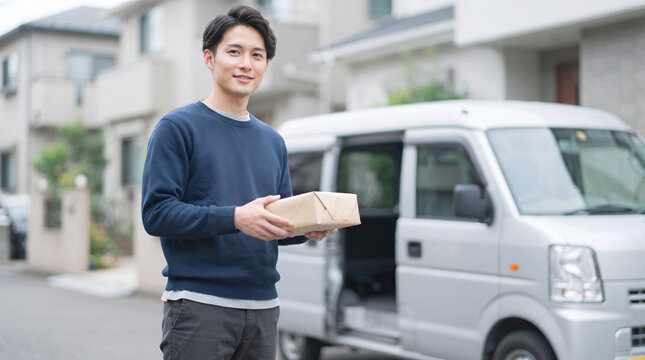 荷物を手にして笑顔で配送作業を行う宅配ドライバーの男性
