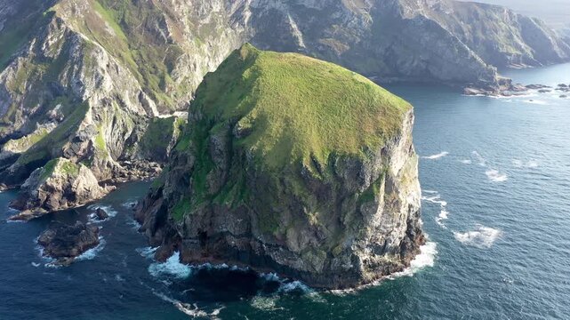 Aerial view of Tormore Island with steep cliffs, grassy summit, and crashing waves in the Atlantic Ocean near Ardara, County Donegal, Ireland.