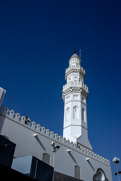 View of the white minaret and ornate parapet of the historic Masjid Quba mosque set against a clear deep blue sky in Madinah, Al Madinah Province, Saudi Arabia.