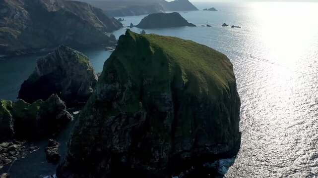 Aerial view of Tormore Island sea stack with rugged cliffs and sunlight reflecting on the Atlantic Ocean in Ardara, County Donegal, Ireland.