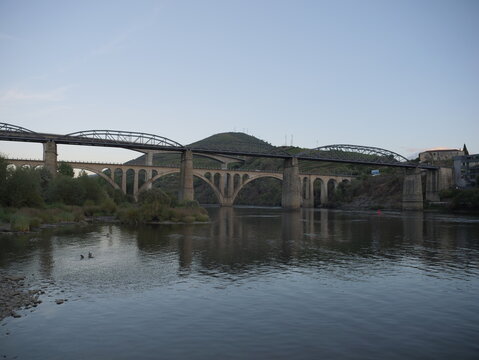 View of the historic bridge spanning the Douro River in Peso da Regua, with rolling hills and calm water under a clear sky in Peso da Regua, Vila Real District, Portugal.
