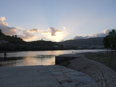 View of the Douro River at sunset with sunbeams breaking through clouds over the terraced hills in Peso da Regua, Vila Real District, Portugal.