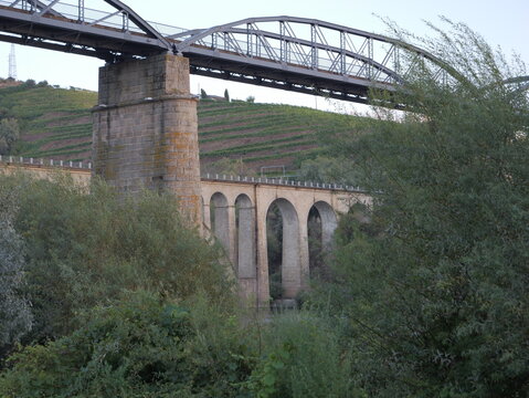 View of the historic stone arch viaduct and metal railway bridge spanning the landscape with terraced vineyards in the background in Peso da Regua, Vila Real District, Portugal.