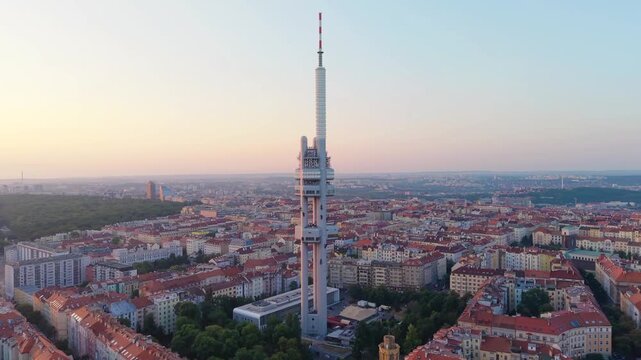 Aerial view of Zizkov Television Tower rising above the historic rooftops and urban landscape during golden hour in Prague, Hlavni mesto Praha, Czechia.