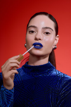 Woman with a blod blue lipstick with a stylish twist on a vibrant red background