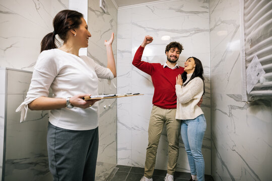 Happy couple celebrating apartment purchase with real estate agent in bathroom