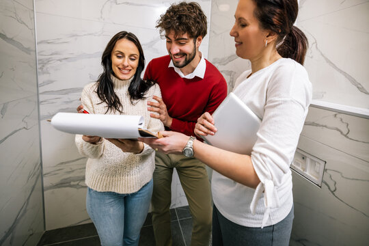 Woman signing property contract on clipboard with realtor and partner watching