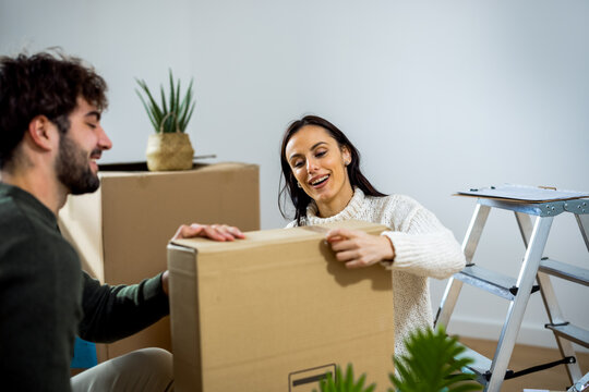 Happy couple sealing cardboard box with hands while moving into apartment