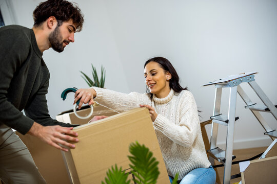 Smiling woman applying adhesive tape to cardboard box with partner at home