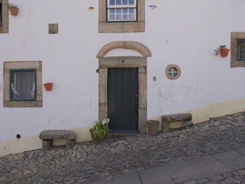 View of a historic stone doorway of a white house with cobblestone street and stone benches in Marvao, Portalegre District, Portugal.