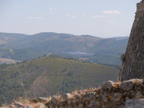 View of the historic stone fortifications of Marvao Castle overlooking the rolling green hills and distant reservoir in the Alentejo region, Marvao, Portalegre District, Portugal.