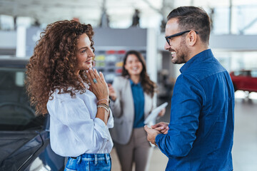 Fototapeta premium Happy Couple Completing New Car Purchase At Modern Dealership With Smiling Salesperson