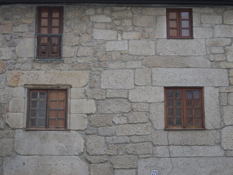 View of a traditional stone wall with three wooden-framed windows in the historic center of Covilha, Castelo Branco District, Portugal.