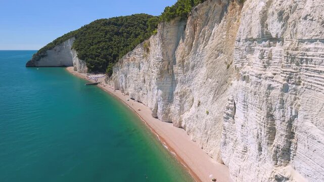Vignanotica one of the best Beaches of Gargano Puglia Italy. vertical white limestone cliff aerial drone flyby empty shore turquoise sea crystal clear water travel 4k video