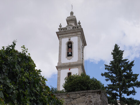 View of the bell tower of the Igreja do Sagrado Coracao de Jesus ou de Sao Tiago rising above a stone wall and lush greenery in Covilha, Castelo Branco, Portugal.