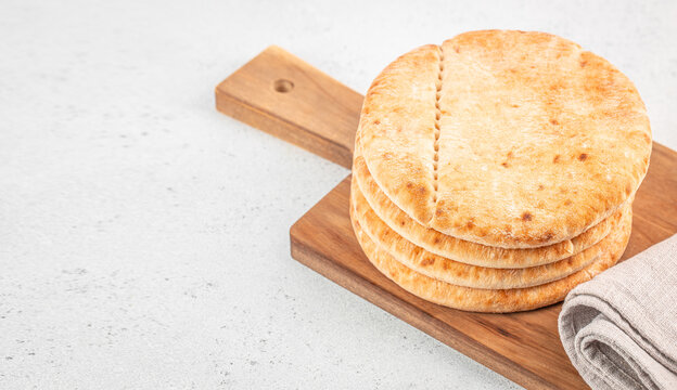 Stack of round flatbreads with toasted spots on wooden cutting board and linen towel, viewed from above on a light textured kitchen surface
