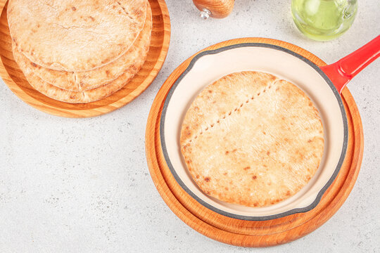 Top view of round flatbreads on wooden plates beside a red handled baking dish and green glassware on a light kitchen surface