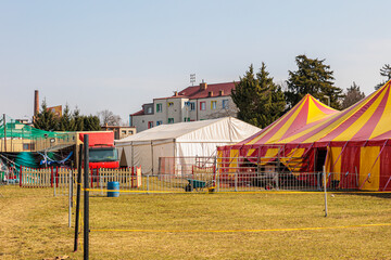 Red and Yellow Circus Tents Behind Picket Fence at Empty Outdoor Carnival Field © Olga