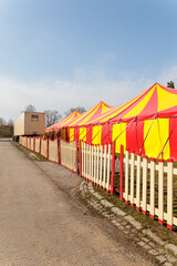 Red and Yellow Circus Tents Behind Picket Fence at Empty Outdoor Carnival Field © Olga