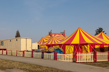 Red and Yellow Circus Tents Behind Picket Fence at Empty Outdoor Carnival Field © Olga