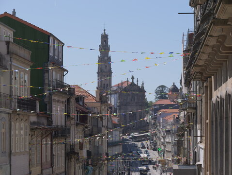 View of the historic Clerigos Church and its iconic tower rising above narrow streets in Porto, adorned with colorful festive bunting between traditional buildings, Porto, Porto District, Portugal.