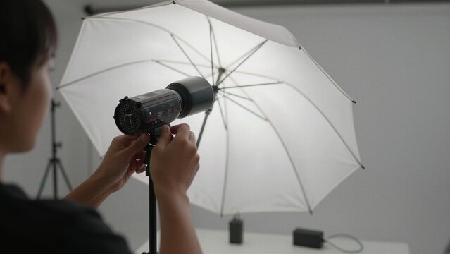A photographer fine-tunes a studio lighting setup with an umbrella modifier for controlled illumination in a professional photo studio environment.