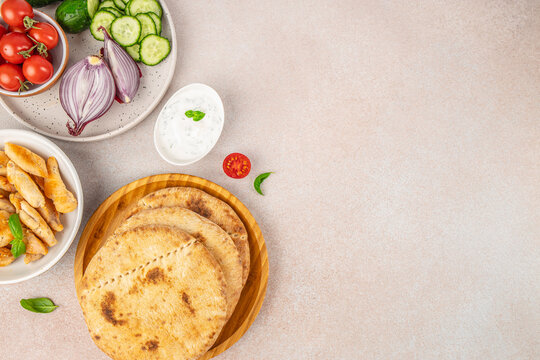 Flat lay of fresh vegetables, creamy dip, grilled flatbreads and fried pastries arranged on a neutral stone surface with copy space for food design