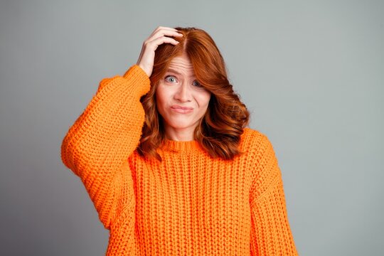 Woman in orange sweater looking confused and unsure with hand on head studio portrait