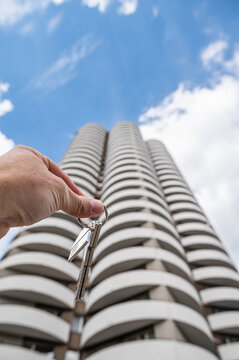 Hand Holding House Keys with Metal House Keychain against Modern Residential Complex Vertical
