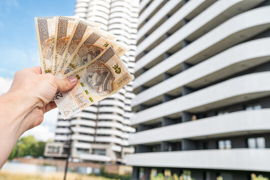 Male Hand Holding Stack of 200 Polish Zloty Banknotes Against Modern Apartment Skyscraper