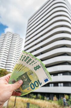 Vertical View of Hand Holding 100 Euro Banknotes Against Modern Apartment Building Exterior