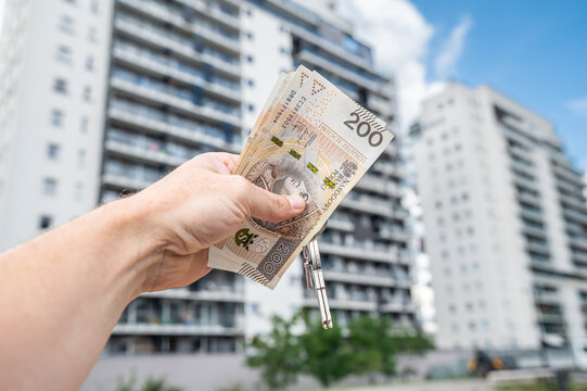 Hand Holding Fan of 200 PLN Polish Zloty Notes and House Key with Modern Buildings Background